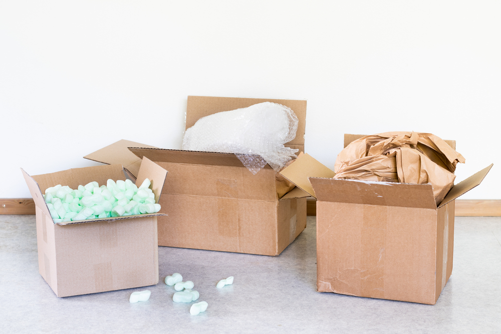 Three open cardboard boxes sit on the floor, one is filled with Expanded PolyStyrene (or commonly known as packing peanuts), one is filled with bubble wrap, and the third is filled with dunnage. - Polystyrene alternatives, EPS Packaging Alternative